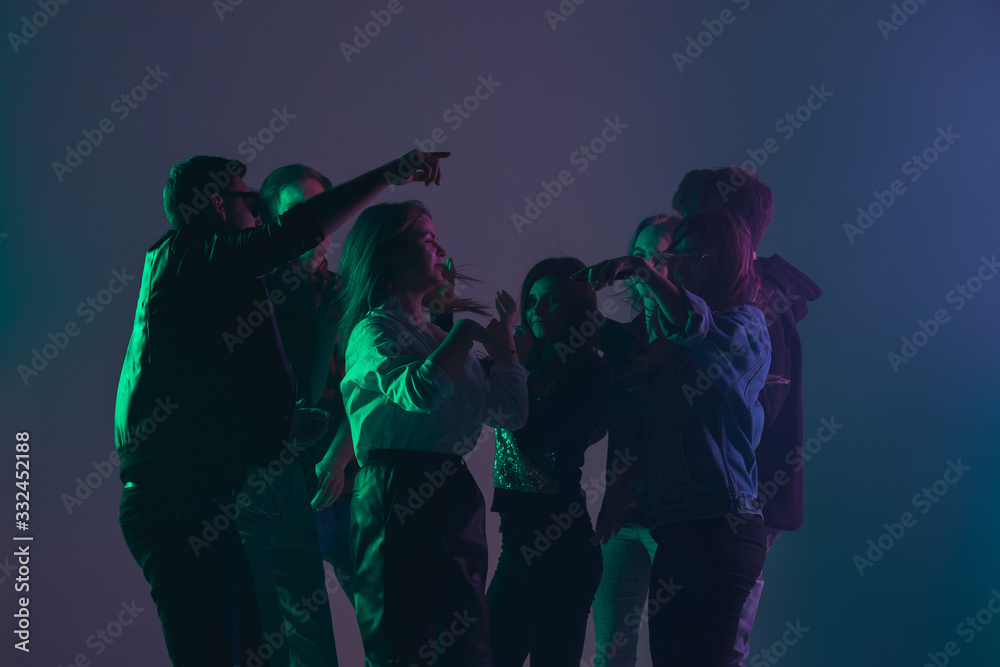 Fototapeta premium Cheering dance party, performance concept. Crowd shadow of people dancing with neon colorful lights raised hands up on dark background. Celebration, holiday, weekend, nightlife and positive vibes.