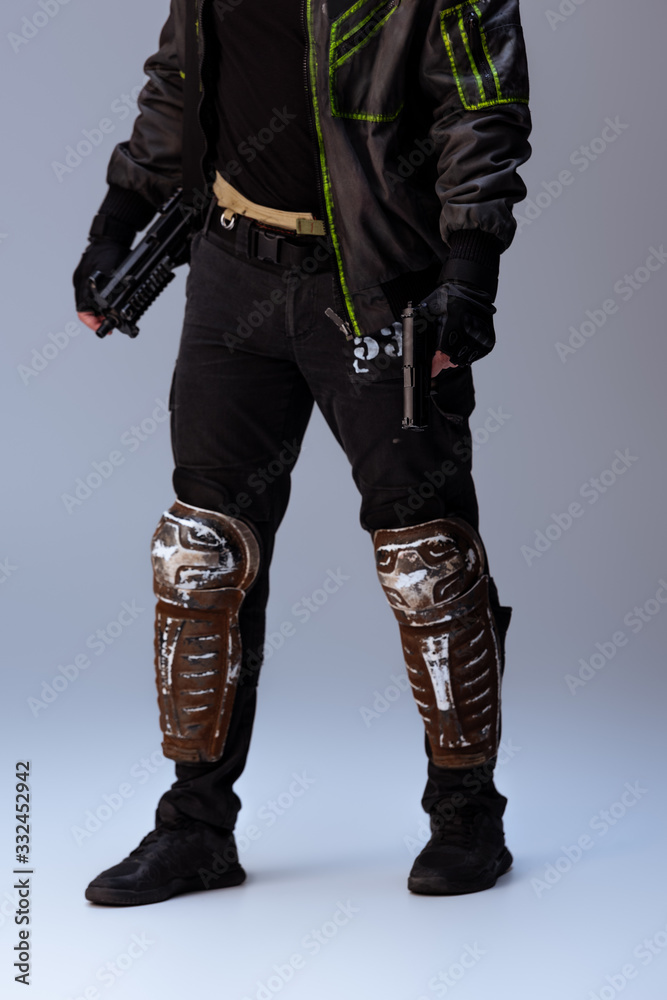 cropped view of cyberpunk player holding gun while standing on grey cropped view of cyberpunk player holding gun while standing on grey