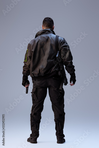 back view of cyberpunk player holding gun and standing on grey