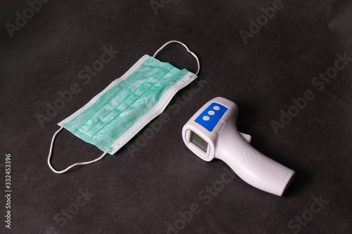 Mask and infrared thermometr on a black background. Coronavirus control, prevention epidemic photo