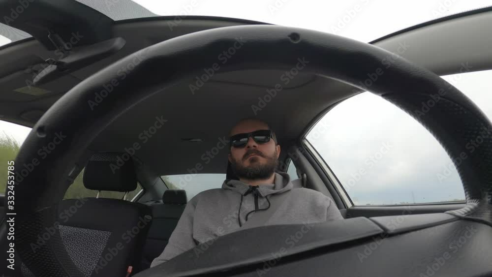 Man in hoodie and with sunglasses driving a car, wide angle view through the steering wheel Man in hoodie and with sunglasses driving a car, wide angle view through the steering wheel