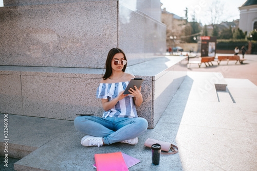 A young caucasian  beautiful girl sits next to a monument with a tablet in her hand © Dragica