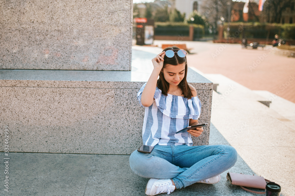 A young caucasian  beautiful girl sits next to a monument with a tablet in her hand