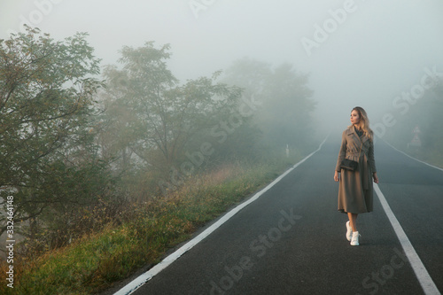 Woman in morning fog is walking along the alley