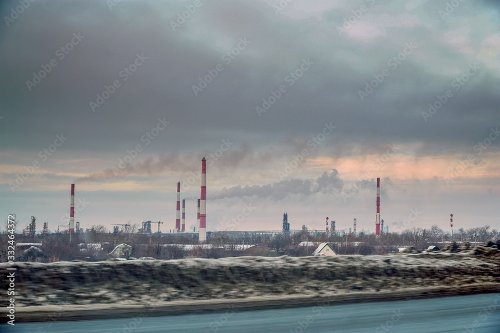 View from the window of a passing car on the Smoking factory chimneys against the overcast sky