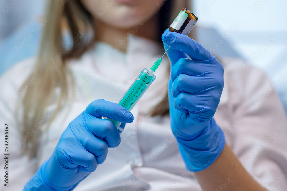 Close up view of medical syringe in rubber blue glove dressed hand, man chest in white medical robe with stethoscope on a blurred background Close up view of medical syringe in rubber blue glove dressed hand, man chest in white medical robe with stethoscope on a blurred background