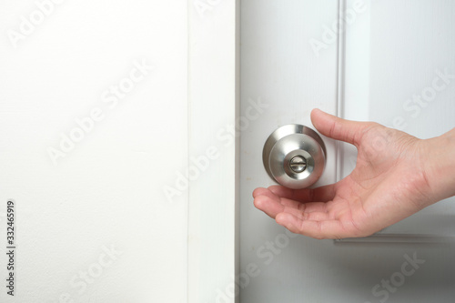 Hand going to hold the doorknobs of the closed white door. Health concept to aware for touching the everyday objects.