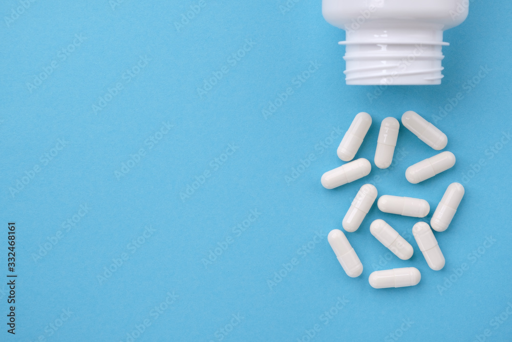White capsules falling from the white bottle on blue paper background. Concept of pharmacy White capsules falling from the white bottle on blue paper background. Concept of pharmacy