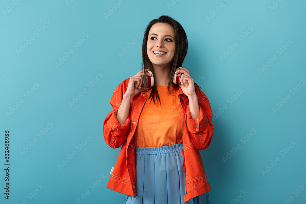smiling woman with headphones looking away on blue background