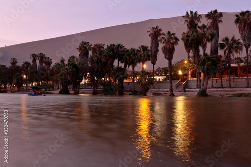 Beautiful view at dusk from the shore of the Huacahina oasis, observing the palm trees, the water and the desert in the blue hour. Ica-Peru photo