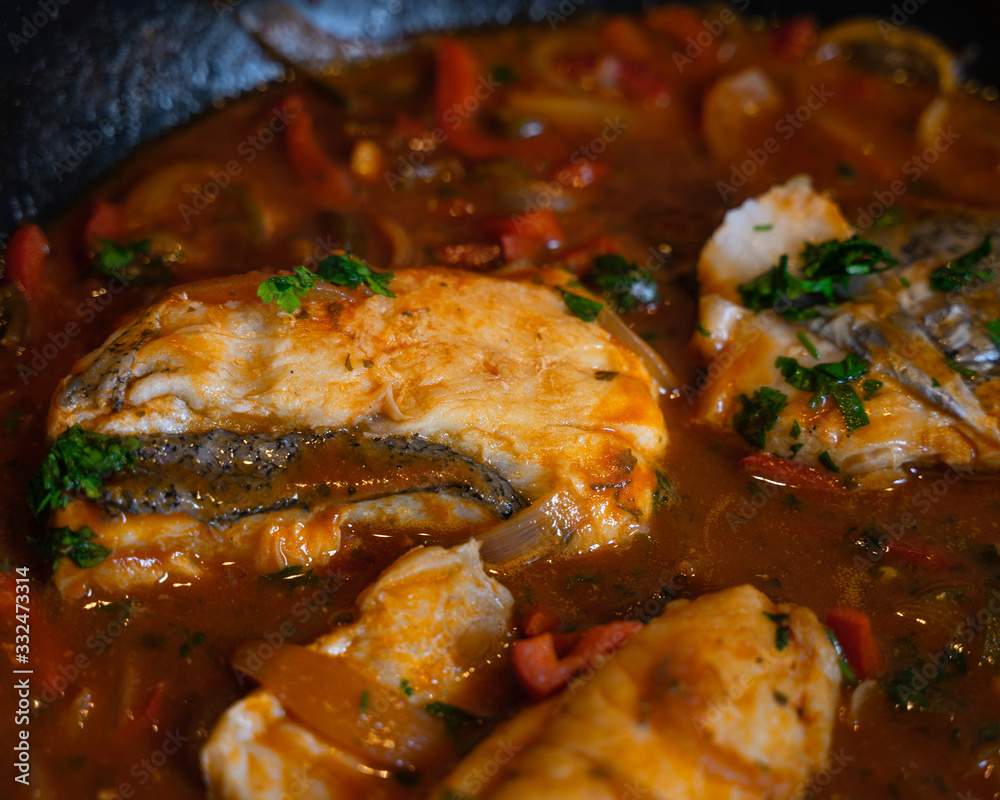 Hake fillet stew, cooking in a tomato sauce with red pepper sauce, with some parsley leaves to garnish Hake fillet stew, cooking in a tomato sauce with red pepper sauce, with some parsley leaves to garnish