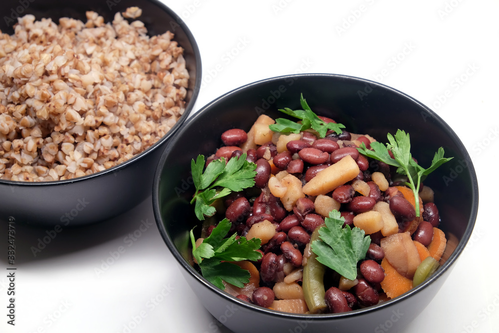 Vegan low calorie lettuce with baked beans with carrots and greens and boiled buckwheat in black round bowls studio shot isolated on white background front view close up