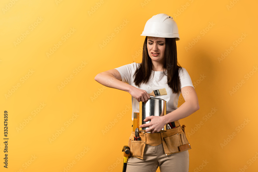 disappointed handywoman opening paint can on yellow background disappointed handywoman opening paint can on yellow background