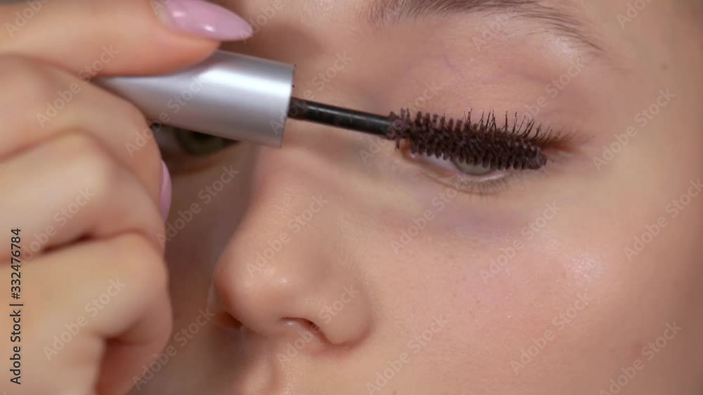 Applying makeup. Young girl looks in the mirror and applies mascara with a brush to the lashes of her eyes. Applying makeup. Young girl looks in the mirror and applies mascara with a brush to the lashes of her eyes.