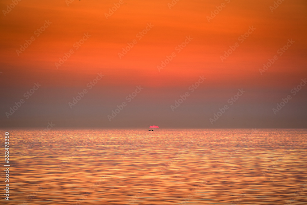 The boat is floating against the backdrop of the rising sun. Golden sunrise at sea.