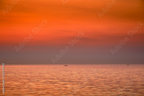 The boat is floating against the backdrop of the rising sun. Golden sunrise at sea.