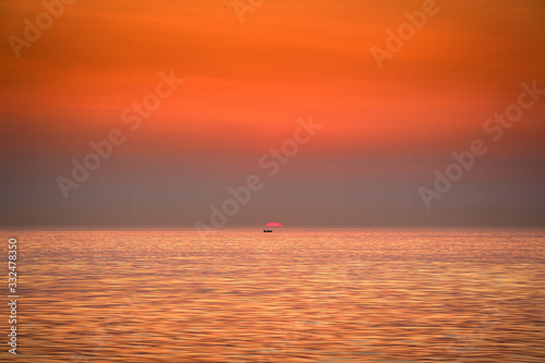 The boat is floating against the backdrop of the rising sun. Golden sunrise at sea.