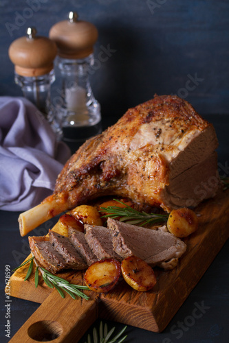 Roast leg of lamb with potatoes and rosemary on dark background. vertical image