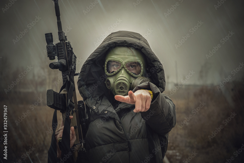 Woman in gas mask with rifle in her hand is showing ahead by her index finger.