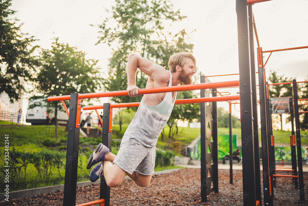 Fototapeta premium Fit Man Workout Out Arms On Dips Horizontal Bars Training Triceps And Biceps Doing Push Ups. Handsome Man Doing Exercise On Parallel Bars. Male Athlete Exercises On Parallel Bars Outdoor