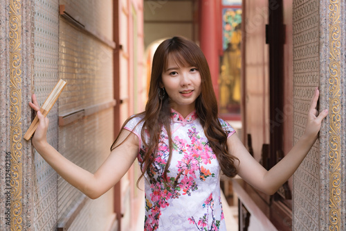 Portrait of Chinese girl wearing Chinese clothes holding paper folding fan in her hand and posing at cement door