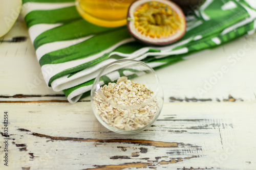 Flattened oats in a neat round glass bowl on an old beautiful table. Close-up. In the background is a beautiful towel  passion fruit and green tea.