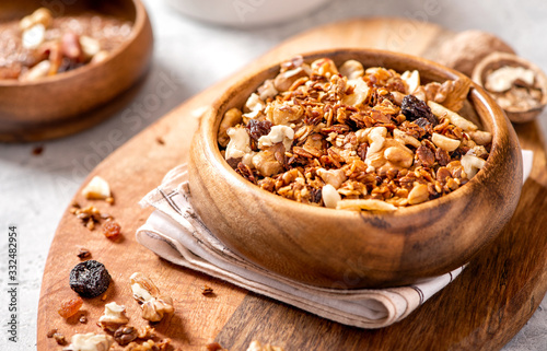 Homemade toasted granola with oats, honey, walnuts, raisins, flax and sesame seeds in a wooden bowl closeup, front view, selective focus. Healthy vegetarian breakfast