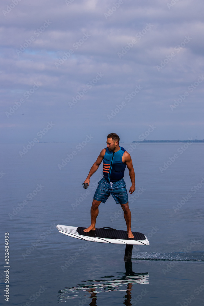 Man riding an electric hydrofoil foil board on a lake with a life jacket