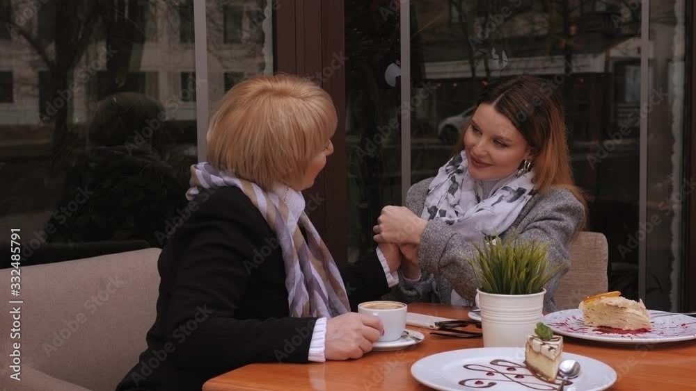 Senior mother sitting in cafe or restaurant with her middle age daughter and enjoying in conversation. Loving adult daughter holds her elderly mother's hand with tenderness. Portrait of a happy family Senior mother sitting in cafe or restaurant with her middle age daughter and enjoying in conversation. Loving adult daughter holds her elderly mother's hand with tenderness. Portrait of a happy family