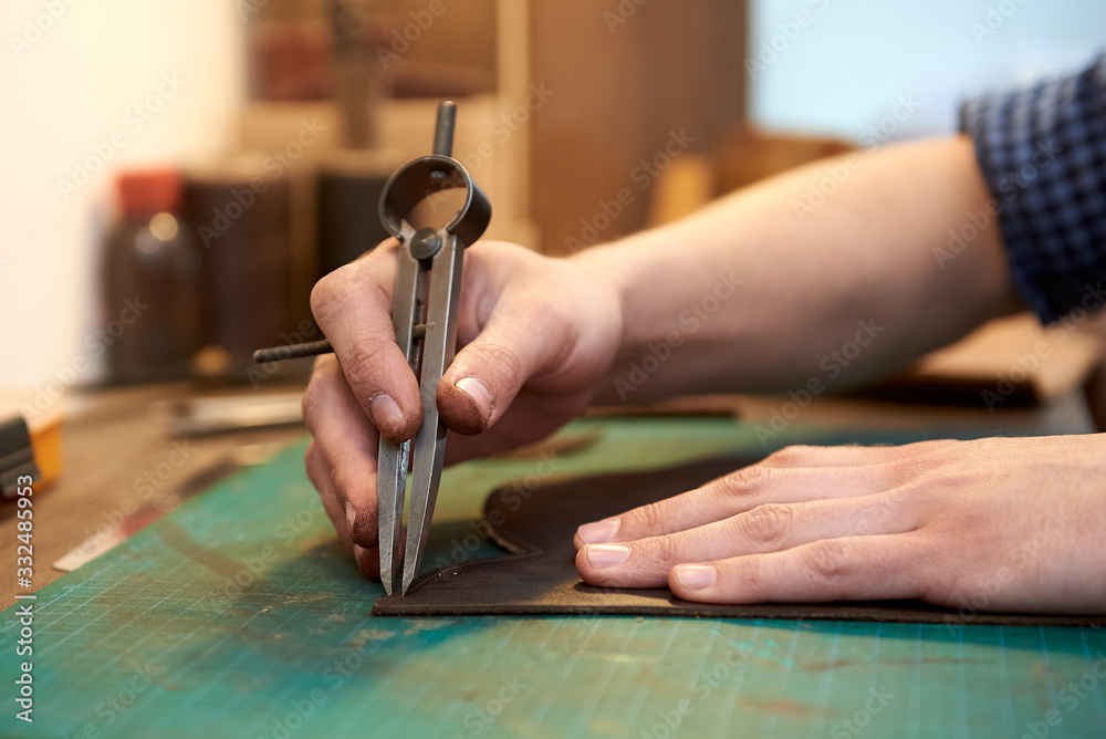 Closeup of skinner craftsman working with brown natural leather using craft tools. The seam width measurement process.