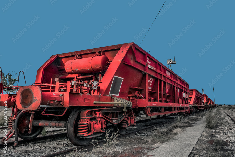 Tren de mercancías de hierro en color rojo varado en una vía férrea. Tren parado en una estación de ferrocarril con cielo azul de fondo. 