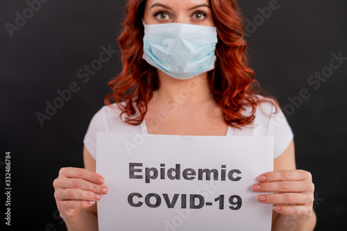 A red-haired woman in a medical mask holds an announcement about the epidemic of Coronavirus. Quarantined. Pandemic of the 21st century. covid-19. photo