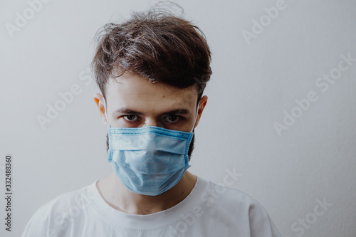 portrait of a young man wearing a protective medical mask and quarantining at home. The concept of voluntary self-isolation of patients and those with coronavirus symptoms © Ananass