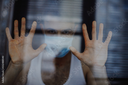 portrait of a young man wearing a protective medical mask and quarantining at home. The concept of voluntary self-isolation of patients and those with coronavirus symptoms