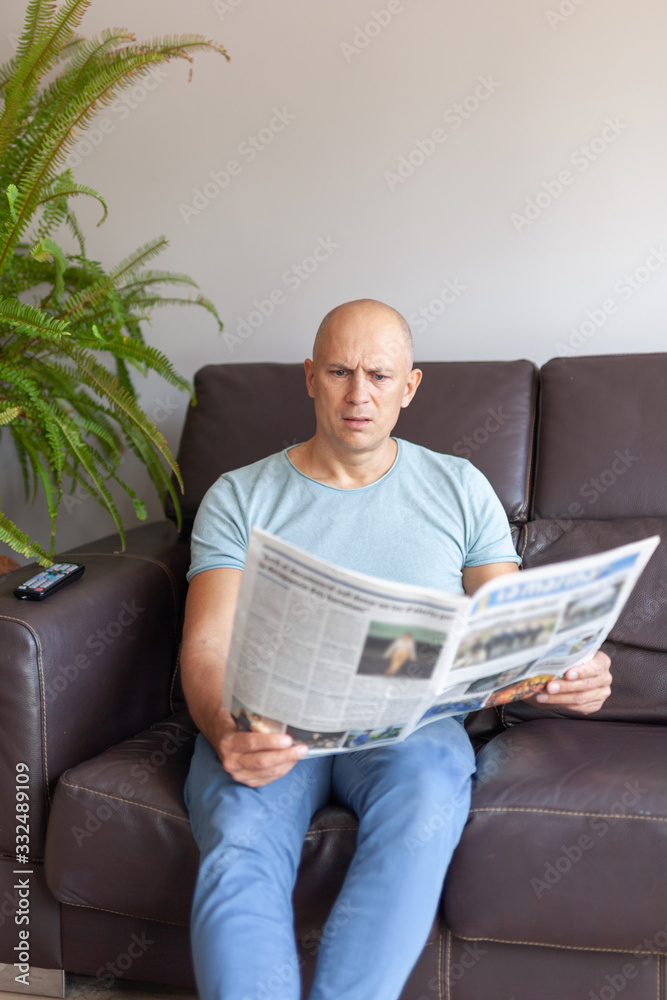 А serious man reading a newspaper at home on the couch А serious man reading a newspaper at home on the couch