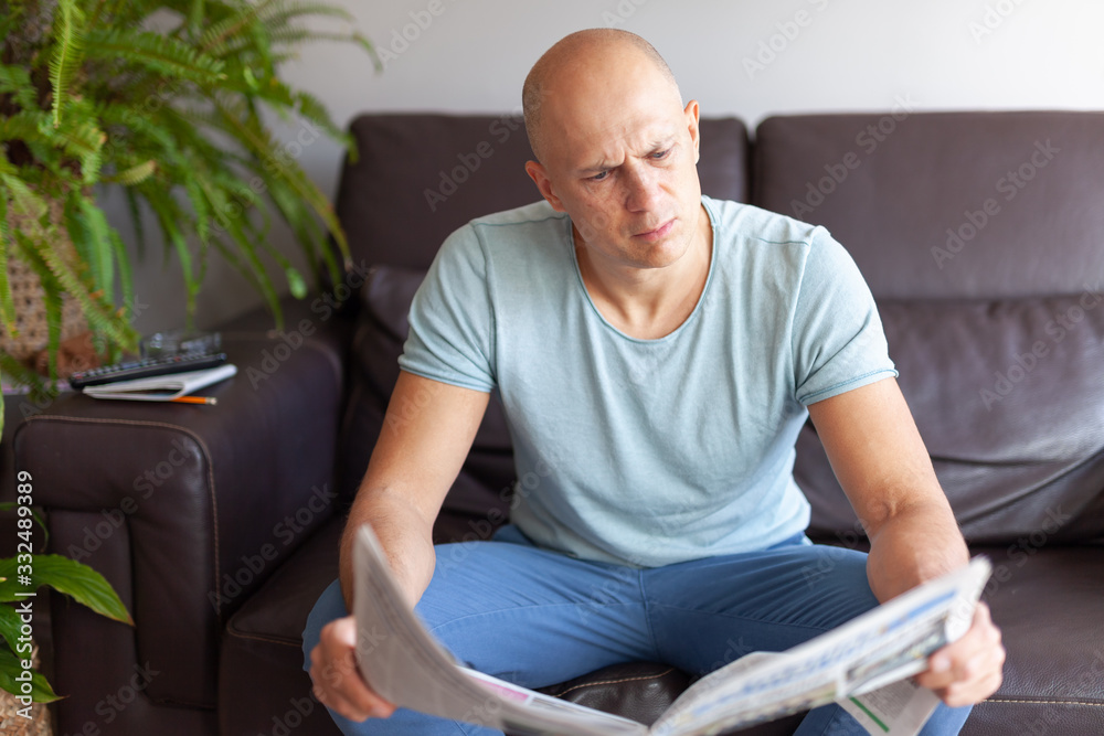 Fototapeta premium А serious man reading a newspaper at home on the couch