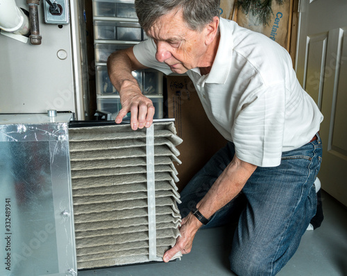Canvas-taulu Senior caucasian man changing a folded dirty air filter in the HVAC furnace syst