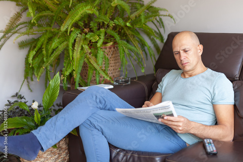 А serious man reading a newspaper at home on the couch