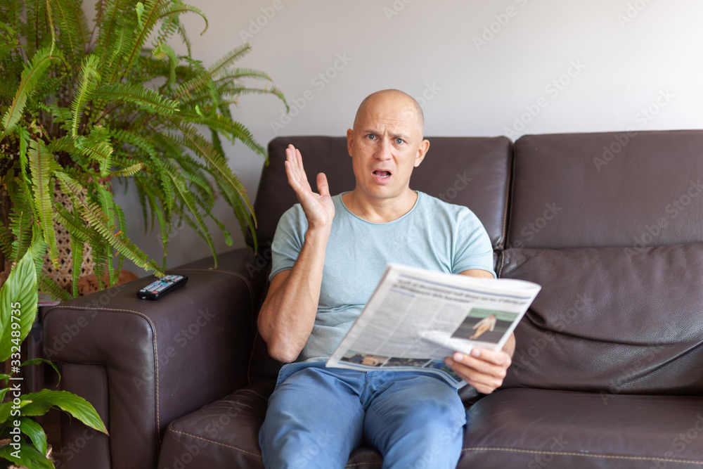 A man at home on the couch reads a newspaper and is very surprised. A man at home on the couch reads a newspaper and is very surprised.
