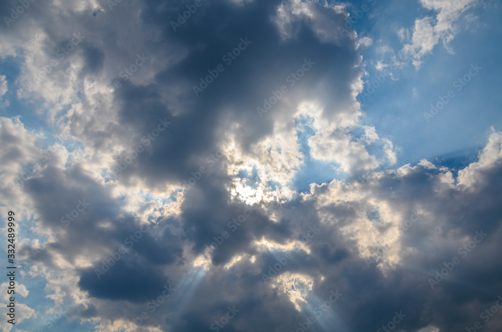 Blue sky with white and gray clouds and sun rays.  Different depth of color and shadow