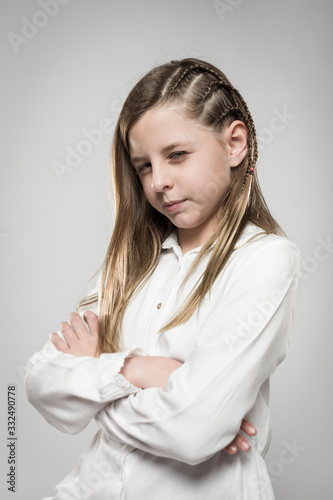 Studio portrait of a cute angry girl with long blonde hair wearing a white shirt against neutral background