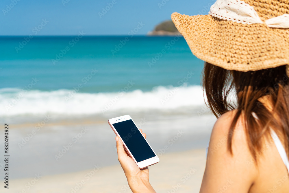 Fototapeta premium Happy traveller Asian woman enjoys at tropical beach while using smart phone on vacation. Summer on beach concept.