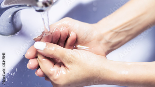 Primer plano levemente elevado de un par de manos de mujer lavandose con jabón sobre una bacha celeste