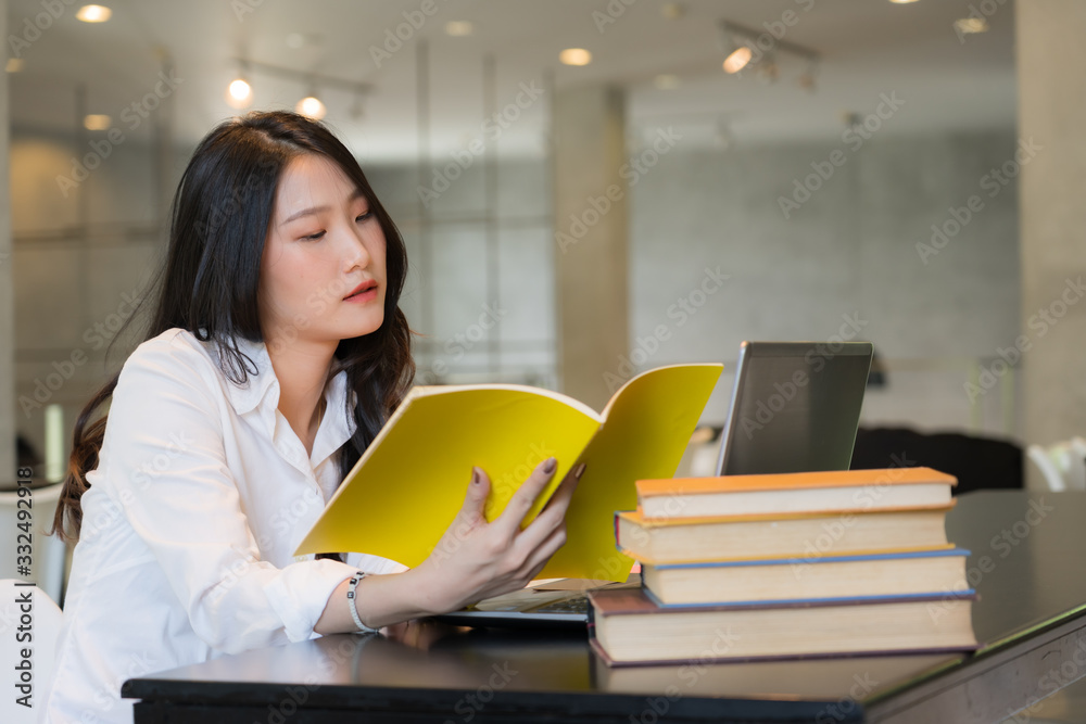 Beautiful student wearing white shirt researching with notebook and books on the table in library Beautiful student wearing white shirt researching with notebook and books on the table in library