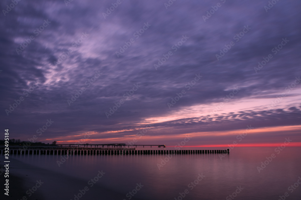 wooden groyne stakes at dawn with colorful evening sky