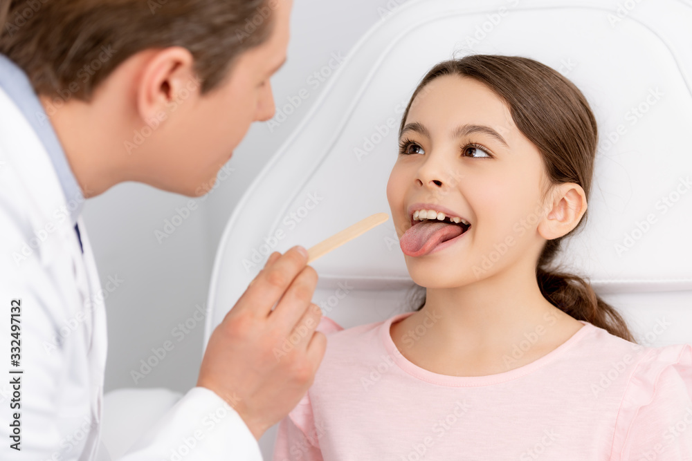 selective focus of ent physician holding tongue depressor near cute kid