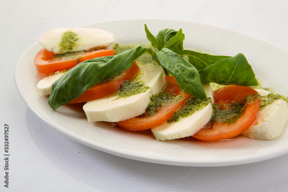 Caprese Salad with Tomatoes, Mozzarella Cheese, Rocket Salad, basil leaves, dressed with Pesto Sauce on rustic wooden background. Traditional Italian cuisine. Flatlay healthy vegetarian dish. Caprese Salad with Tomatoes, Mozzarella Cheese, Rocket Salad, basil leaves, dressed with Pesto Sauce on rustic wooden background. Traditional Italian cuisine. Flatlay healthy vegetarian dish.