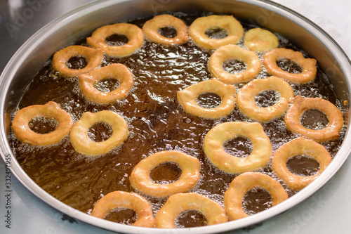 Small donuts being deep fried in boiling oil in a large pan, at a street food market, top view or flat lay photo of healthy food photographed with selective focus