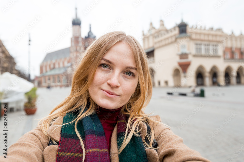 Stylish blonde woman tourist making selfie photo in front of the famous St. Mary's Basilica on the Market square. Travel concept and discovery of beautiful places. Krakow, Poland Stylish blonde woman tourist making selfie photo in front of the famous St. Mary's Basilica on the Market square. Travel concept and discovery of beautiful places. Krakow, Poland