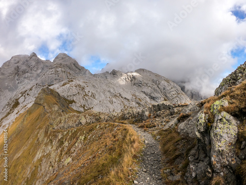 A pathway leading to high peaks in Italian Alps. Sharp slopes on both sides of the valley. Hard to reach mountain peaks. There are many mountain ranges in the back. Serenity and peace. Autumn vibes © Chris